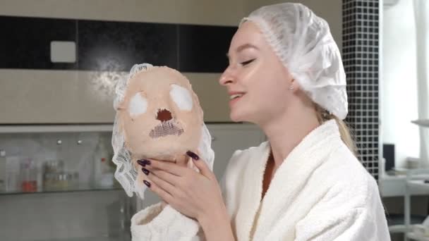 Portrét krásné ženy s kalenou alginátovou maskou v rukou s úsměvem a radostným smíchem na kosmetické klinice. Koncept krásy, kosmetiky, zdravotní péče, módy a péče o pleť. 4K — Stock video
