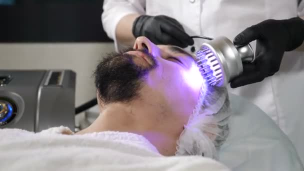 Junger gutaussehender Mann bekommt Kosmetikbehandlung im Schönheitssalon. Hardware-Kosmetologie. Anti-Aging und Anti-Falten-Apparat Kosmetologie. Moderne Entspannungsbehandlung. 4 k Filmmaterial — Stockvideo