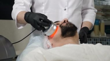 Güzellik salonunda kozmetik dersi alan yakışıklı bir adam. Donanım kozmetolojisi. Yaşlanma önleyici ve kırışıklık önleyici kozmetoloji. Modern rahatlatıcı tedavi. 4k görüntü