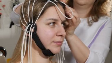 Doktor kadın hastaya elektronik sensörler bağlıyor. Genç bir kadın EEG makinesine ya da elektroansefalografa bağlı. Beyin elektriksel aktivitesinin grafiksel kaydını üretiyor.