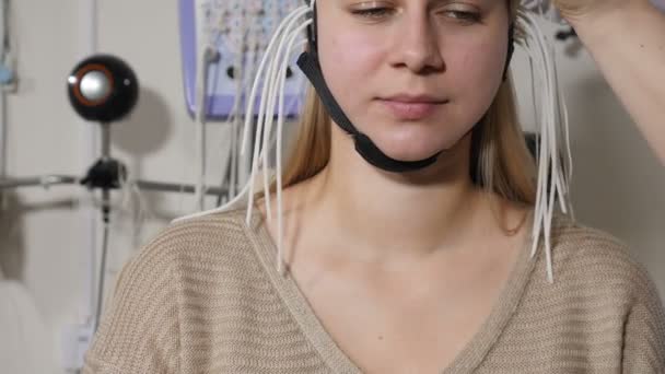 Mujer joven que acude a la clínica para evaluación neurológica utilizando la máquina EEG. Doctora operando electroencefalografía durante la prueba en la paciente. Diagnóstico de epilepsia en forma médica en la clínica — Vídeos de Stock