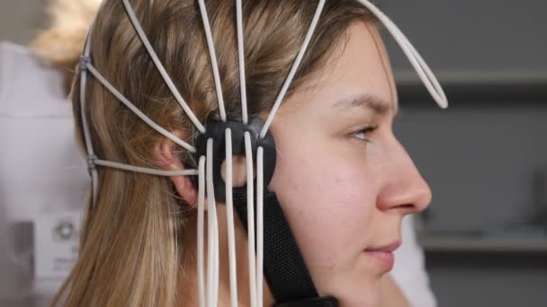 Arzt verbindet elektronische Sensoren mit Drähten zur Patientin. Junge Frau wird an EEG-Maschine oder Elektroenzephalograph angeschlossen, der die elektrische Aktivität des Gehirns grafisch aufzeichnet — Stockvideo