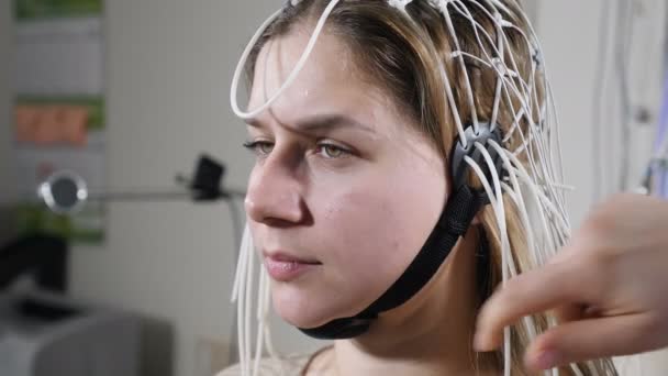 Mujer joven que acude a la clínica para evaluación neurológica utilizando la máquina EEG. Doctora operando electroencefalografía durante la prueba en la paciente. Diagnóstico de epilepsia en forma médica en la clínica — Vídeos de Stock