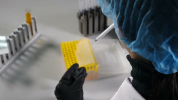 Back view of female scientist dropping chemical liquid in test tubes. Close up of scientist hands working with chemical reagents in laboratory glassware. 4k — Stock Video