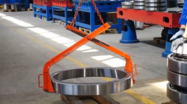 Fabrika deposunda çalışan, mavi üniforma giyen, vinç kullanan, vinç kullanan, büyük yuvarlak metal parçalarını vinç demeti ile kaldıran erkek işçilerin arka görüntüsü. 4k görüntü