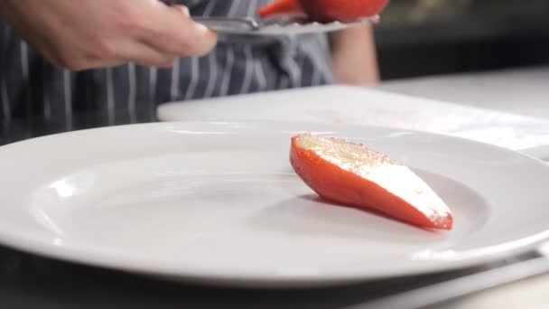 Concept gastronomique. Gros plan du chef masculin qui met avec des pinces sur une assiette délicieux dessrt de poire rouge cuit dans le vin. Des images au ralenti. Cuisiner dans un restaurant français. Poires rouges sur coupe blanche — Video