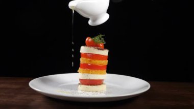 Mozzarella salatasına yavaş çekimde zeytinyağı dökmek. yemek görüntüleri siyah arkaplanda. Peynirli İtalyan Caprese salatası. Sağlıklı gıda ve vejetaryen konsepti. Tam Hd