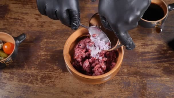 Kitchen in restaurant, food video, slow motion. Close-up shot of male chef in black gloves preparing gourmet dish of meat tartare and mixing salad ingredientsin bowl. Full hd — Stock Video