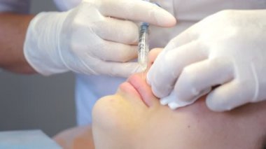 Kadın doktor-kozmetik uzmanı dudaklarına iğne yapıyor. Güzellik ve kozmetoloji kavramı. Yan görüş. Kozmetik uzmanı estetik ameliyat yapıyor. 4k görüntü