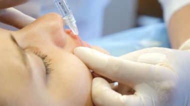 Güzellik kliniği. Eldivenli güzellik uzmanı kadın dudaklarına yaşlanma önleyici iğne yapıyor. Genç bir kadın güzellik yüz kozmetolojisi prosedürünü uyguluyor. Kolajen enjeksiyonları. 4K 'da çekilmiş.