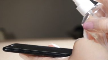 İşlem, temizlik ve sterilizasyon konsepti. Virüs ve bakterilere karşı telefon dezenfeksiyonu. Cep telefonunu temizlemek için ıslak mendil ve dezenfektan kullanan koruyucu eldivenli bir kadının yakın plan fotoğrafı.
