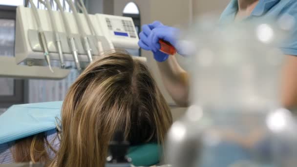 Dental treatment concept. Close-up shot of female dentist working in clinic. Back view. Cosmetic dentistry veneers. Female doctor putting yellow glasses on patient and taking dental drill from — Stock Video