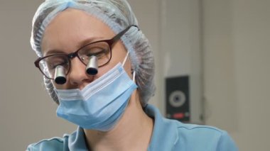 Diş tedavisi sırasında genç dişçiye dürbünü büyüten gözlüklere yakından bakın. Dürbünlü ortodontist, göz ameliyatı yapıyor. 4k görüntü