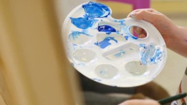 Sanat eserleri. Boyama işleminin yakın çekimi. Parlak ışıklandırılmış odada, tuvale akrilik boya sürmüş güzel bir çocuk resmi. El fırçasının yakın plan görüntüsü. Tam Hd