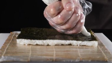 Suşi ustası yemek yapıyor. Yavaş çekimde krema soslu şef garnitürü. Lezzetli börekler satışa ve yemeğe hazırlanıyor. Siyah arka planda yavaş çekim yemek videosu. Suşi yuvarlama işlemi. Eller kapalı.