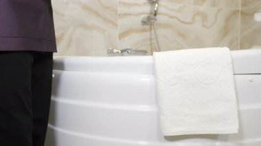 Modern otel ya da konut binasında temizlik hizmeti. Oteldeki ya da temizlik şirketindeki hizmetçilerin küvete beyaz havlu koyarken yakın plan çekimleri. Banyo misafirler için hazır. 4k görüntü