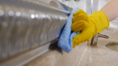 Hizmetçi servisi. Temizlik konsepti. Lastik eldivenli hizmetçi duvarda seramik fayansları bez ve temizlik malzemesiyle yıkıyor. Otel personelinden üniformalı ve koruyucu eldivenli genç bir kadın.