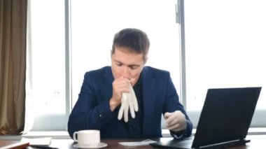 Yakışıklı, komik bir iş adamı. Panoramik pencerelerin önünde parlak bir ofiste otururken lastik eldiven üflüyor. Corona virüsü varken ofis hayatı. Salgının sonu. 4k video