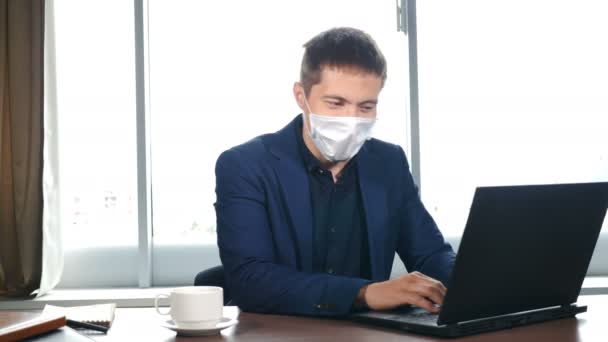 Retrato del oficinista en el lugar de trabajo con portátil en la mesa con quitar la máscara facial médica y hace que la respiración profunda. Fin de la cuarentena y pandemia de Coronavirus. Hombre quitándose la máscara. Vídeo 4k — Vídeos de Stock