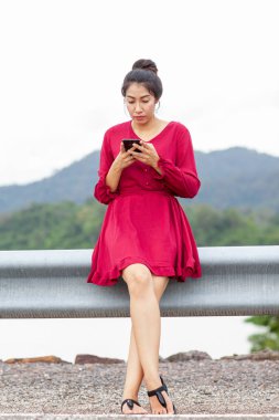 Korkulukta oturan ve akıllı telefon kullanan genç Asyalı kadın.