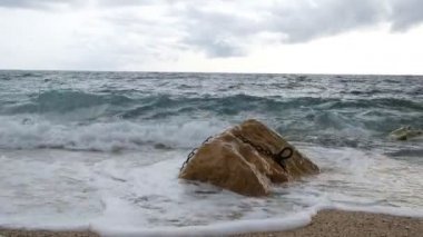 Akdeniz 'de sonbahar günü deniz dalgaları. Dalgalar, metal bir zincirin bağlı olduğu büyük bir kayaya çarpar. Suyun basıncıyla zincir sallanıyor. Cassis. Provence. Fransa. 4k.