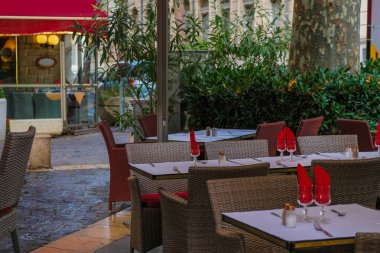 Avignon. Provence. Fransa. 25 Ekim. 2019. Avignon 'un Eski Şehir Meydanı' ndaki yeşillikler arasında boş restoran masaları. Masalarda kırmızı peçeteler ve kırmızı restoran şemsiyesi. Gıda Turizmi.