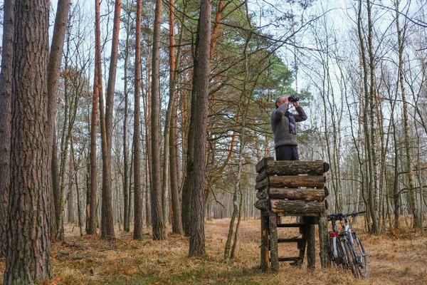 59歳の男が双眼鏡を見ている ウクライナの森の中の木造狩猟塔の男 塔のそばに自転車が立っている 自己分離概念 — ストック写真