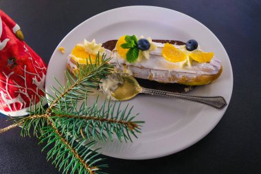 Beyaz tabakta kremalı krema. Pasta yabanmersini, mandalina dilimleri ve nane yapraklarıyla süslenmiş. Kremalı bir kaşığın üstünde. Bayram havası Noel geyiği ve ladin dalı tarafından yaratılmıştır..