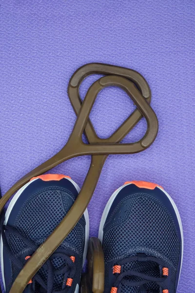 Rubber expander for fitness and blue sneakers on a purple exercise mat. Copy space. Vertical image.
