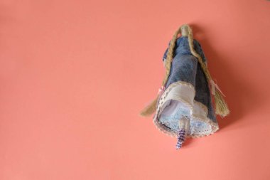 Uçan etekli kumaştan yapılmış komik bir cep bebeği ve mercan zemininde uzun keten örgüler. Uzayı kopyala Kapatın. Minimalizm. El işi üretim konsepti.