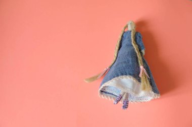  Mercan zemininde uzun keten örgülü kumaştan yapılmış komik bir cep bebeği. Uzayı kopyala Kapatın. Minimalizm. El işi üretim konsepti.