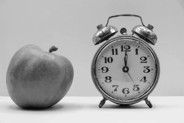 Black and white photo. Apple with vintage alarm clock in Ukraine. Concept time for yourself.