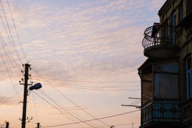 Ukrayna, Lutsk 'ta eski evin siluetlerinin arka planında pembe akşam gökyüzü şekilli balkon ve elektrik kablolu fener. Boşluğu kopyala.