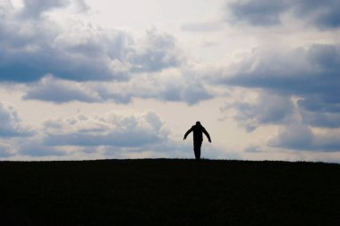 Ukrayna 'da bulutların ardında tepenin üstünde yürüyen bir adamın silueti. Başarı hedefi konsepti. Kişisel izolasyon kavramı.