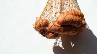 Beyaz arka planda turuncu bir hasır çantanın içindeki sosisler. Parlak güneşin berrak gölgeleri.