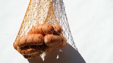 Beyaz arka planda turuncu bir hasır çantanın içindeki sosisler. Parlak güneşin berrak gölgeleri.