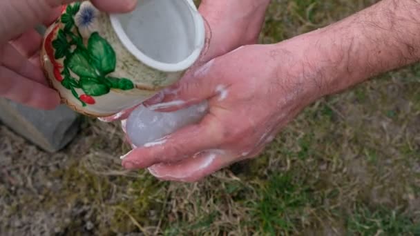 男は緑の草を背景に石鹸で手を洗う 陶器の鍋から水を注ぐ — ストック動画