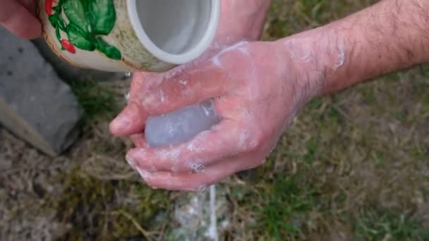 男人在绿草的背景上用肥皂洗手 水是从瓷壶里倒出来的 — 图库视频影像