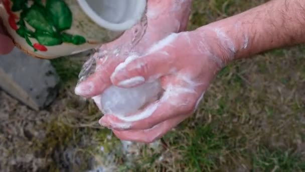 男は緑の草を背景に石鹸で手を洗う 陶器の鍋から水を注ぐ — ストック動画