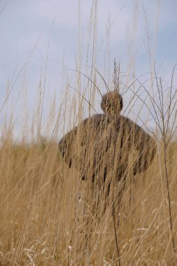 Ukrayna 'nın vahşi doğasında, uzun kuru çimlerin arkasında siyah elbiseli bir adamın silueti. Yürüteçin arkasında siyah bir sırt çantası var. Boşluğu kopyala.
