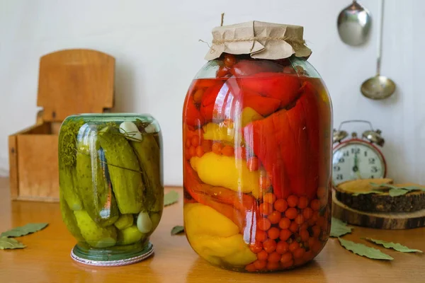 Rustic still life with pickled vegetables, a vintage alarm clock and an old wooden chest for salt on a white background. Appetizing pickles and paprika with red currant tomatoes.