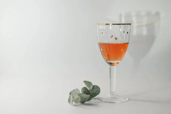 Vintage wine glass with rose wine and a branch of eucalyptus on a white background. On the wall is a reflection from a wine glass. Copy space.