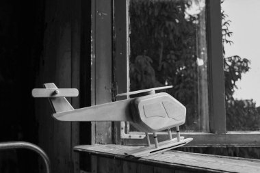 Ukrayna 'da eski bir ahşap evin pencere eşiğinde oyuncak tahta bir helikopter. Uçuş konsepti. Uzayı kopyala Siyah ve beyaz resim.