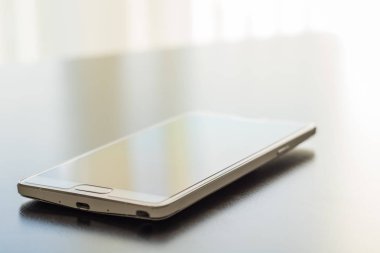 Bir koyu parlak masaüstü yüzeyinde beyaz cep telefonu