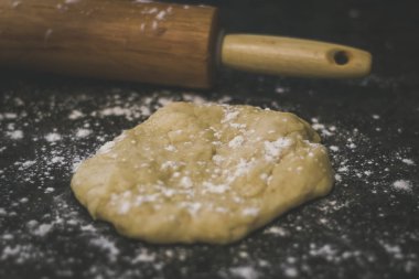 Taze ev yapımı hamur--dan tırmalamak yapılıyor. Hamur merdane ile silindir dışarı sürecindedir. Hamur ve sayaç top un serpilir. 