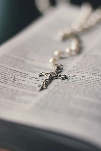 銀とパールの数珠ネックレスは聖書で開いているページの中央に配置されます 画像のフォーカスが開いたページの真ん中にある十字架ペンダント上の場所 ストックフォト
