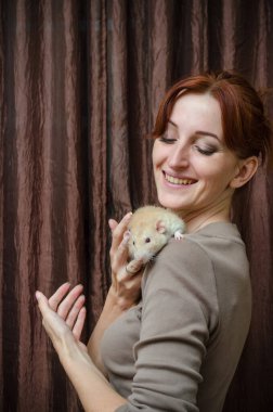 Mutlu, gülümseyen, kızıl saçlı, kahverengi arka planda gri bir fare tutan kız. Yeni yılın sembolü.