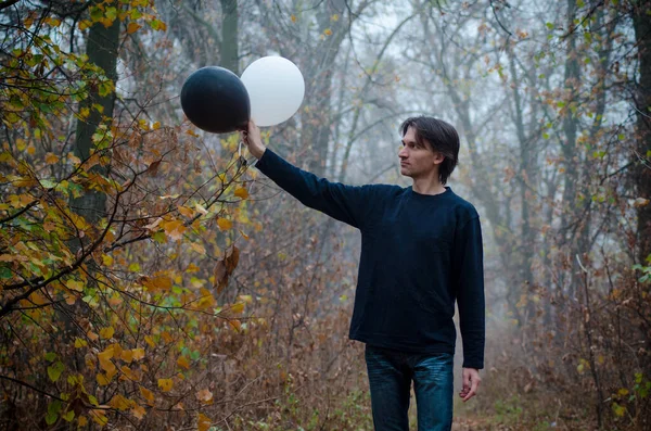 Sisli sonbahar ormanındaki adam elindeki siyah beyaz balona bakar, iyi ve kötü kavramı, seçim yapar, yakın plan. — Stok fotoğraf