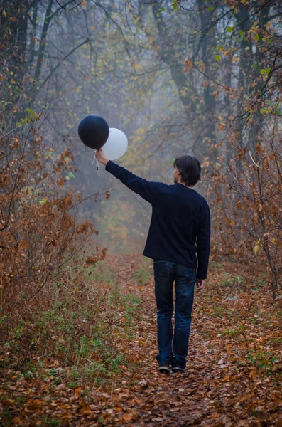 Man in foggy autumn forest looks at black and white balloon in his hand, thinks about life, good and evil, makes choice