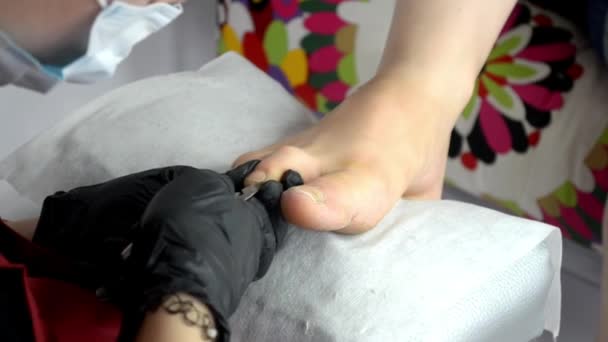 Мастер педикюр в черных перчатках удаляет избыток кожи, ногти на ногтях ножницами — стоковое видео